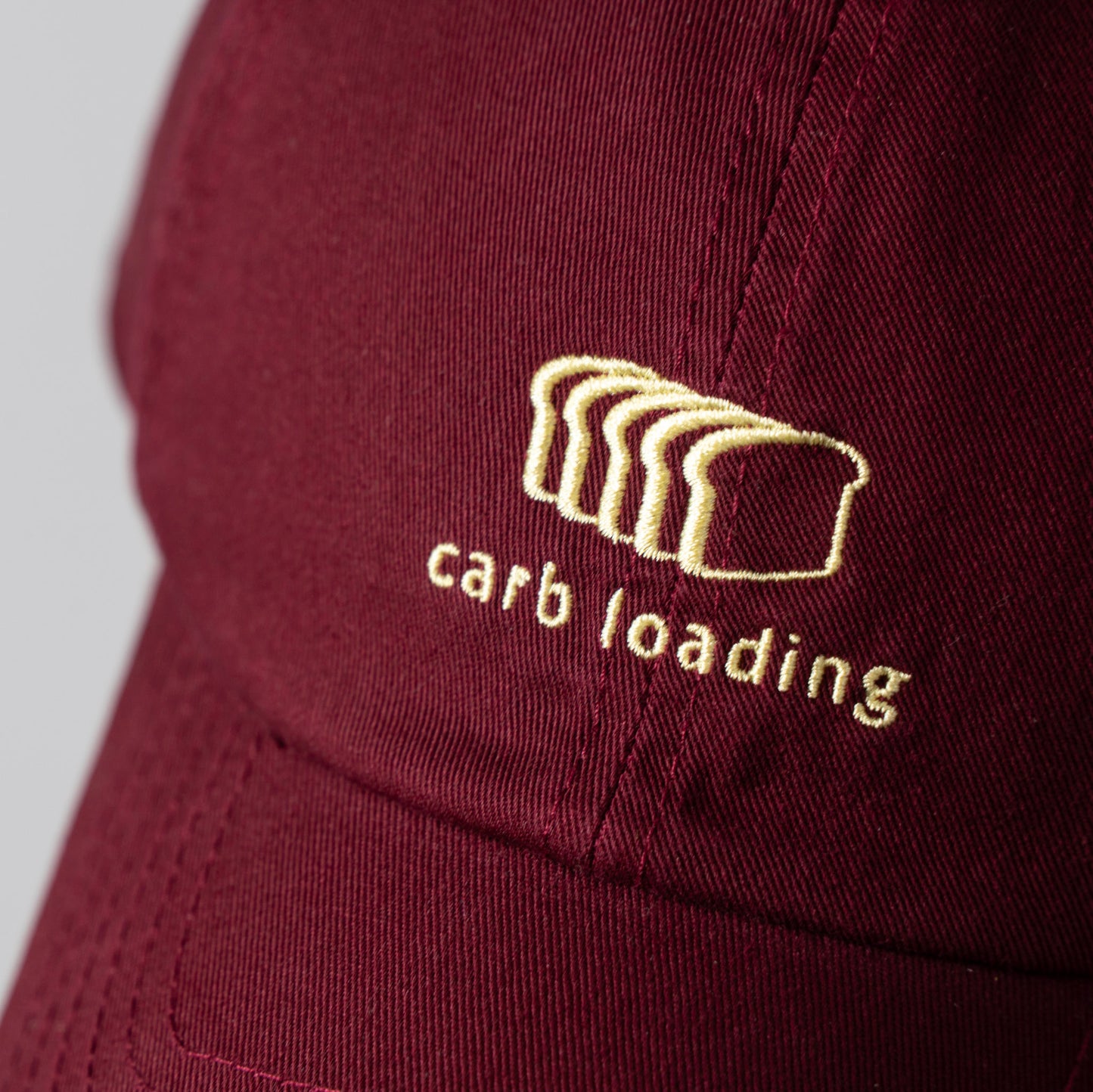 A maroon cap with embroidered bread slices and 'carb loading' text