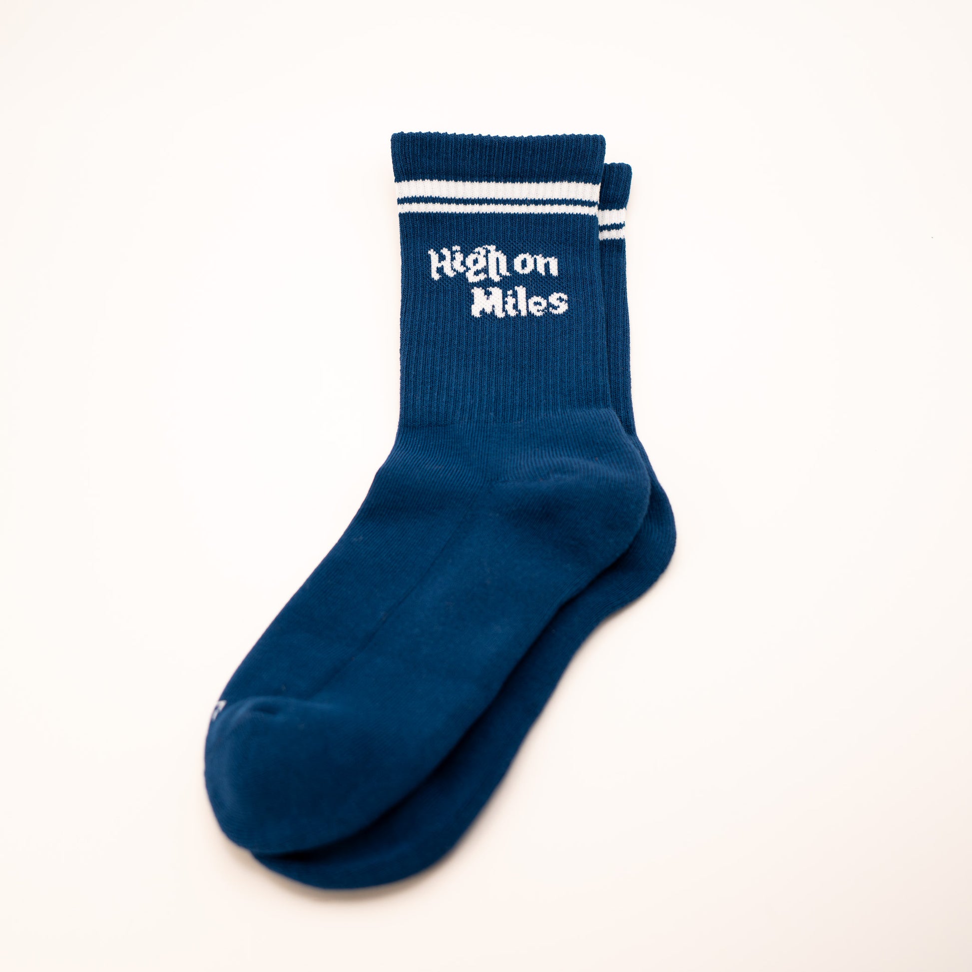 A pair of navy blue crew socks with white stripes and 'High on Miles' printed in white on the cuff, displayed on a clean off-white background.