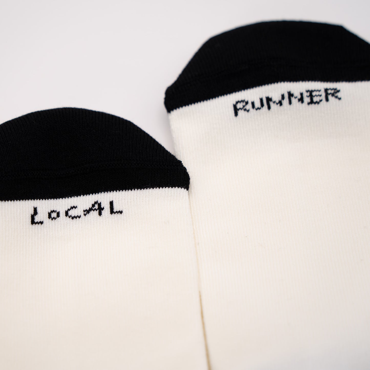 Two off-white crew socks with black toe caps, featuring the words 'LOCAL' and 'RUNNER' printed in black pixel-style text near the cuff, displayed on a clean white background.