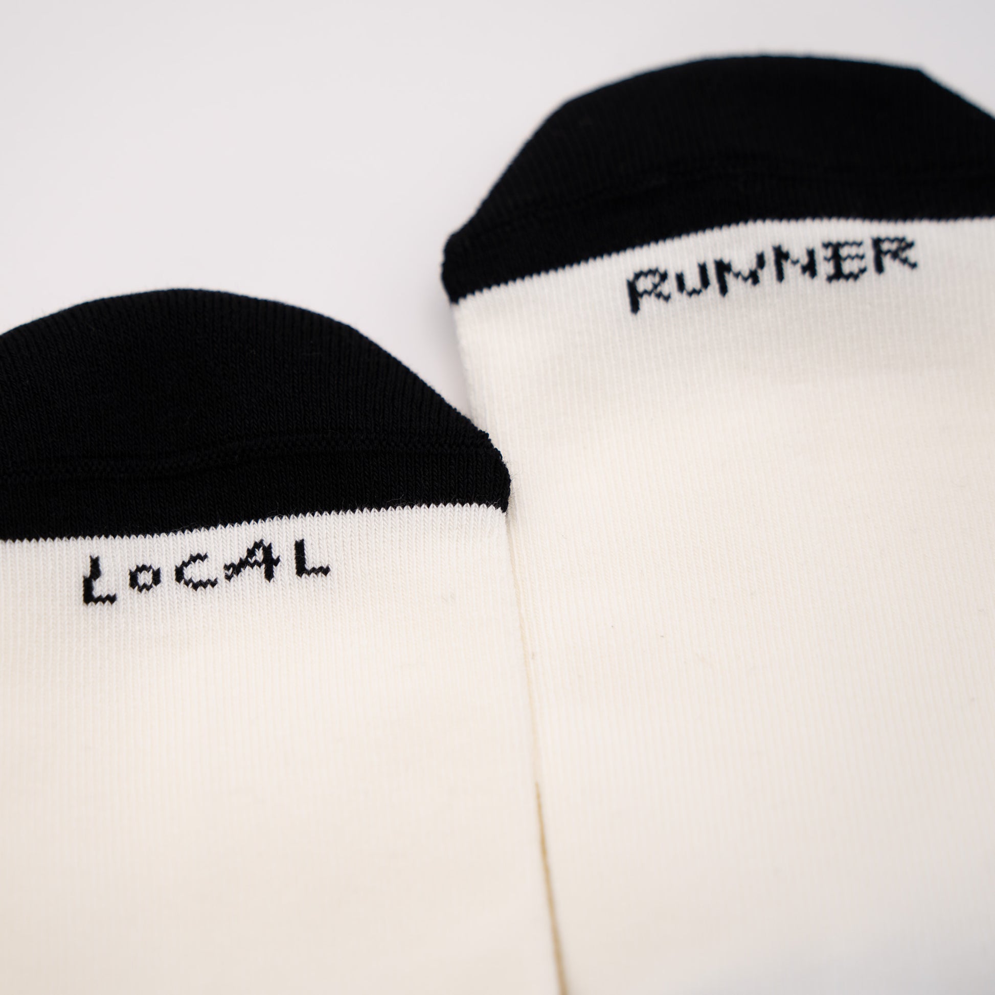 Two off-white crew socks with black toe caps, featuring the words 'LOCAL' and 'RUNNER' printed in black pixel-style text near the cuff, displayed on a clean white background.