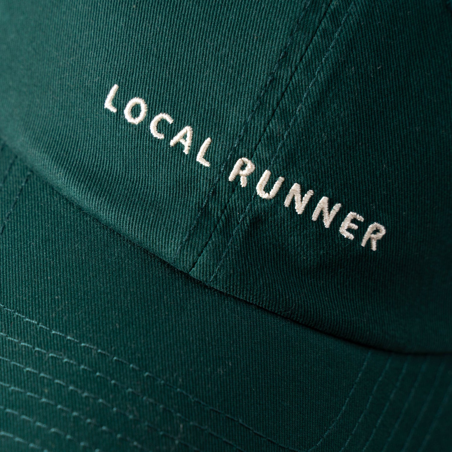 A dark green cap with 'LOCAL RUNNER' embroidered on it
