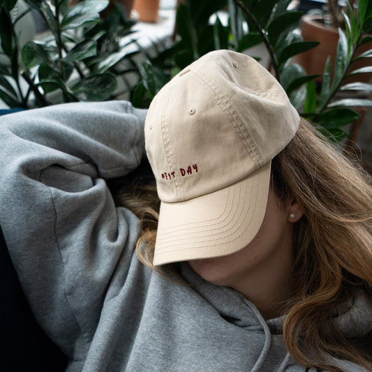 A beige cap with Rest Day embroidery, indoors with plants