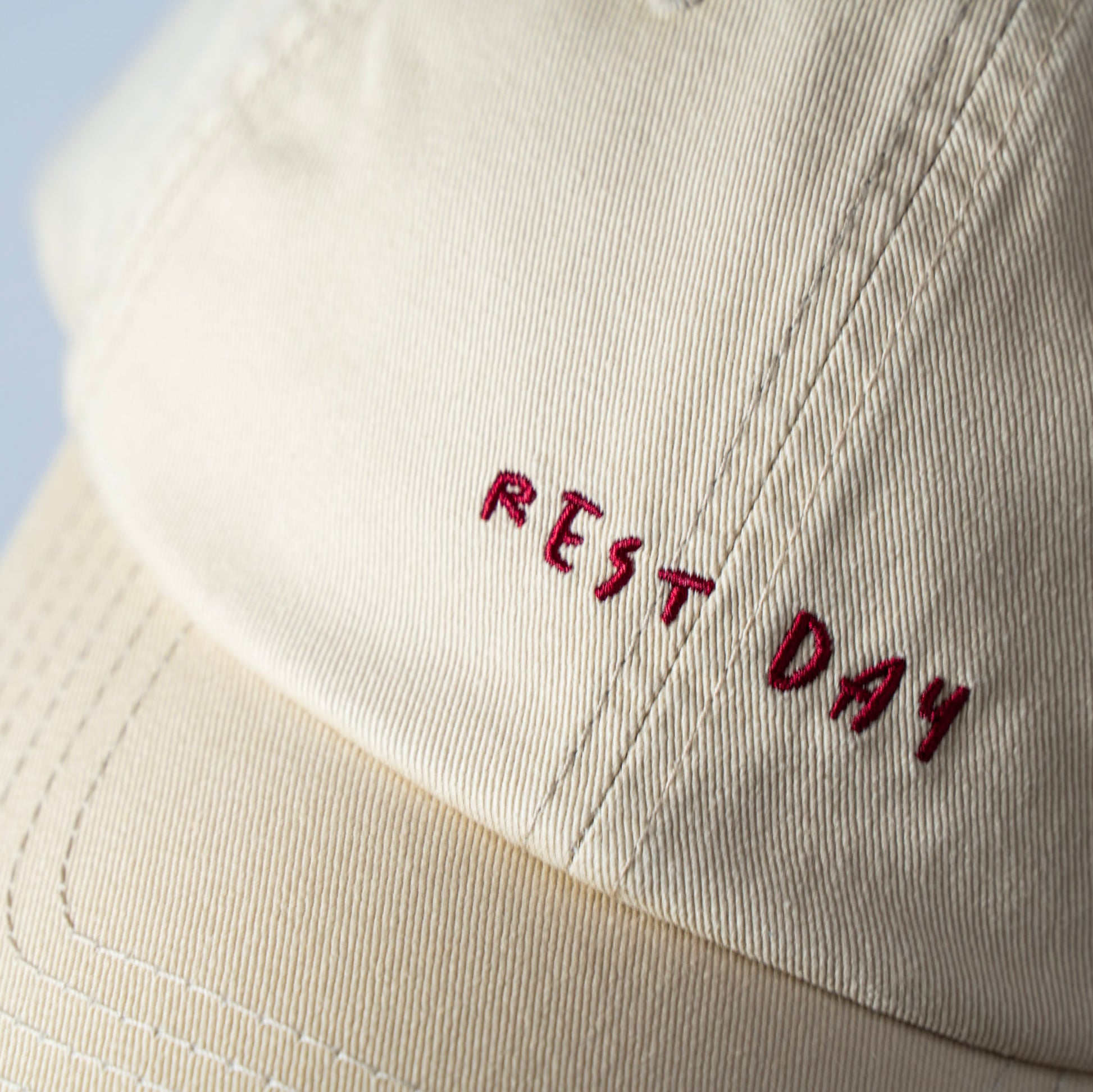 A beige cap with 'REST DAY' embroidered in maroon