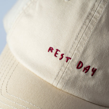 A beige cap with 'REST DAY' embroidered in maroon